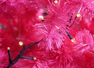 A string of Christmas lights rests on bright pink branches of a Christmas tree that's obviously artificial.