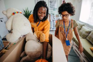 Two Black women pack toys into a box, as though preparing a donation