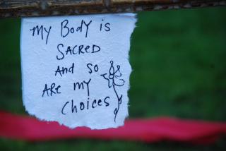 A hand-written sign says, "My body is sacred and so are my choices."
