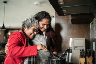 A Latinx mother and daughter embracing while cooking in the kitchen at home
