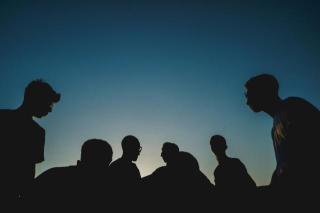 A silhouette of six or seven young people against a cloudless sky, which ranges from pale blue near the bottom to deep blue at the top of the image.