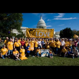 A crowd of people wearing 'Standing on the Side of Love' (SSL) t-shirts gathered in front of the U.S. Capitol, holding up a large SSL banner and several smaller signs.