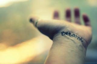 An open hand stretches out, the word "breathe" written or tattooed on the wrist