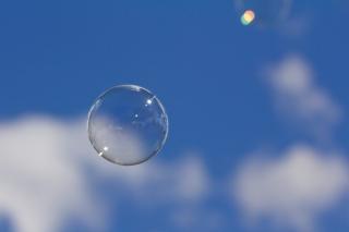 A perfectly spherical bubble floats in front of a blue sky and puffy white clouds