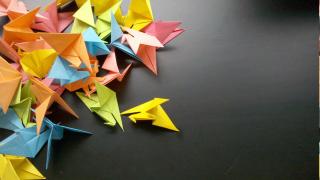 A pile of paper cranes, in different colors, on a black surface
