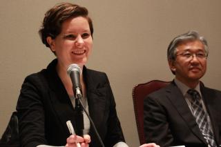 Ray Acheson, at left, smiles and speaks into a microphone. To her right sits Hiro Sakurai, another panelist.