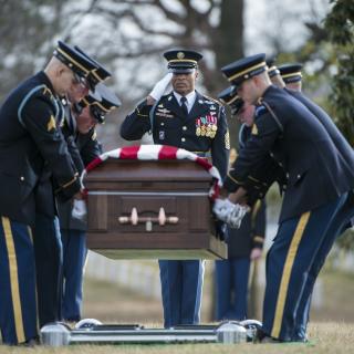 A U.S. Army Honor Guard in dress uniform lower a coffin into the ground.