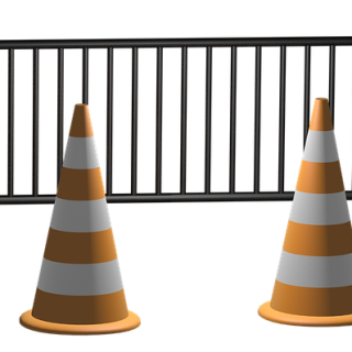 Two striped traffic cones in front of a traffic fence