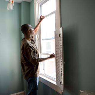 A person reaches up to the sill of a window, as if fixing or cleaning the window.