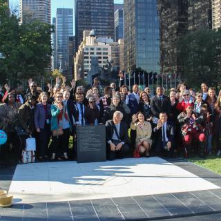 A crowd of people standing around a stone plaque on the ground that honors the commitment to end poverty