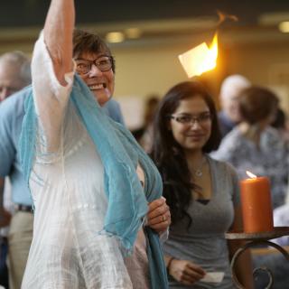 A piece of brightly flaming flash paper hangs suspended in midair as a parishioner, arm lifted, looks on in wonder.