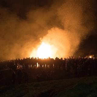 A large number of people are in silhouette against the blaze of a bonfire