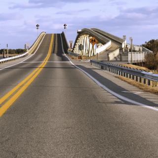 A two lane highway rises on to a steep bridge.