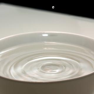 A tiny drop of water bouncing off of the surface of water in a bowl.