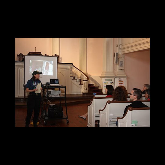 A Unitarian Universalist presents photographs on a screen to others in pews. Photo by Michael Sheridan.