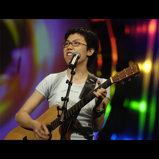 A guitarist, playing and singing into a microphone in front of a colorful light show. Photo by Nancy Pierce.