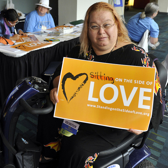 A woman in an electric scooter proudly displays her 'Sitting on the Side of Love' placard. Photo by Nancy Pierce.