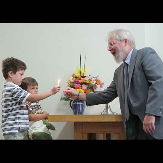 Two children pass a lit candle to Brian Griffin, for lighting the chalice on the table beside them. Photo by Karen Krogh.