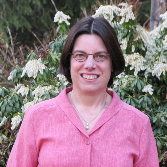 Gail Forsyth-Vail, smiling in front of a rhododendron for an outdoor headshot. Photo courtesy Gail Forsyth-Vail.