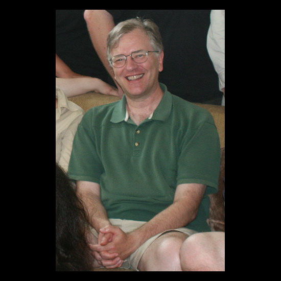 Doug Muder, smiling as he sits on a sofa in an informal picture. Photo by Helio Fred Garcia.