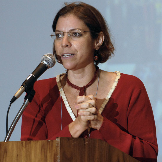 Maria Rodriguez, hands clasped, speaking into a microphone. Photo by Nancy Pierce.