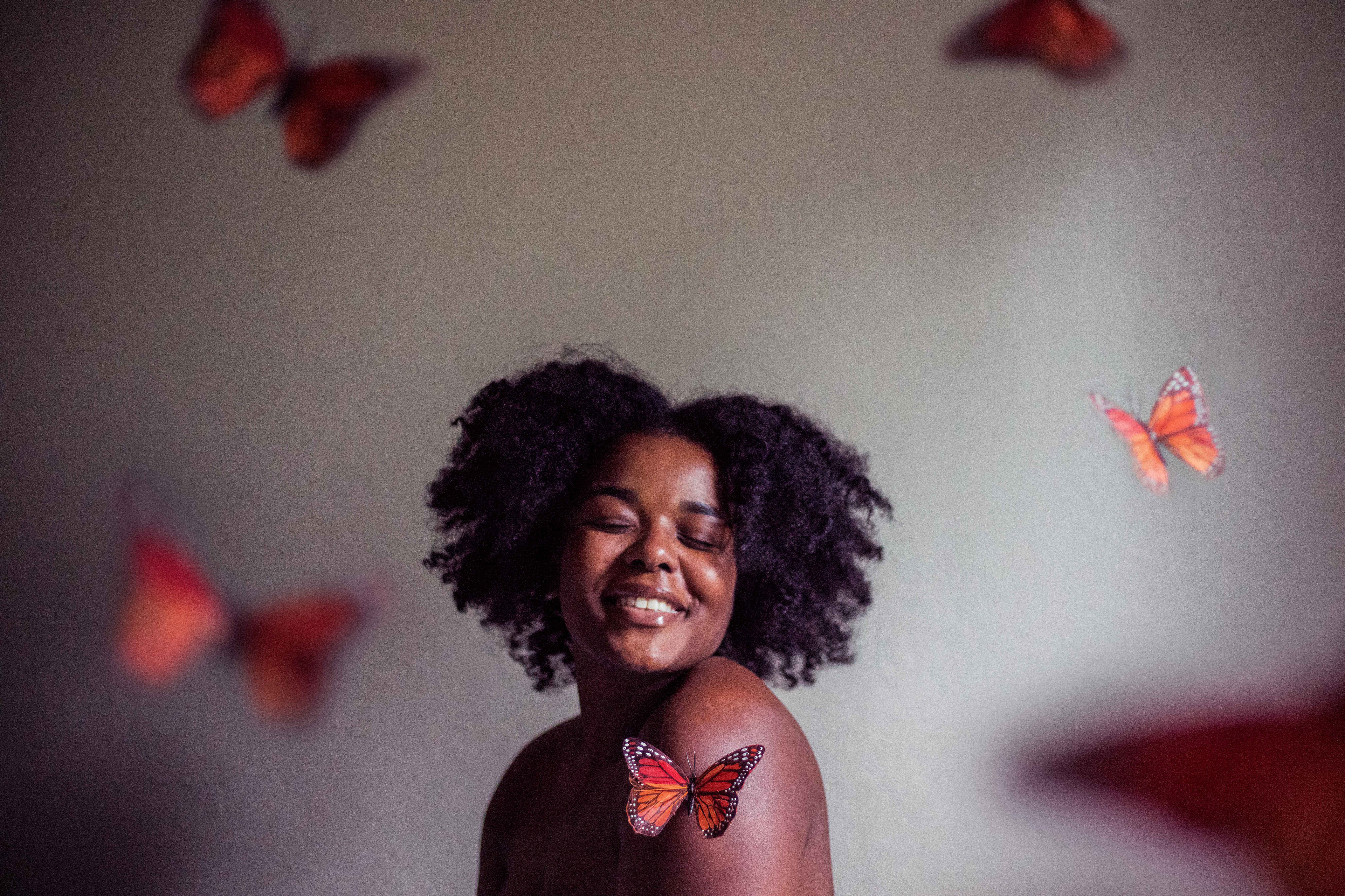A Black woman smiles, as she is surrounded by a ring of monarch butterflies.