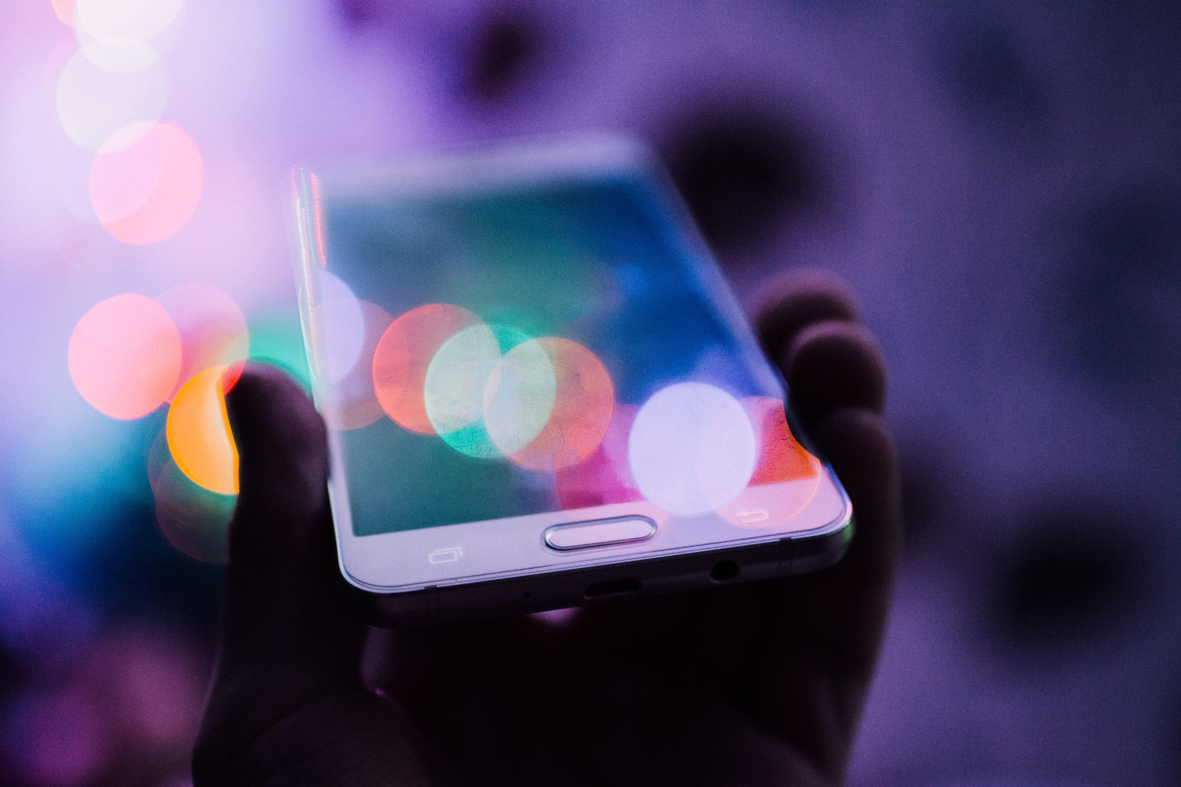 A person holds a smartphone, whose screen reflects colorful lights