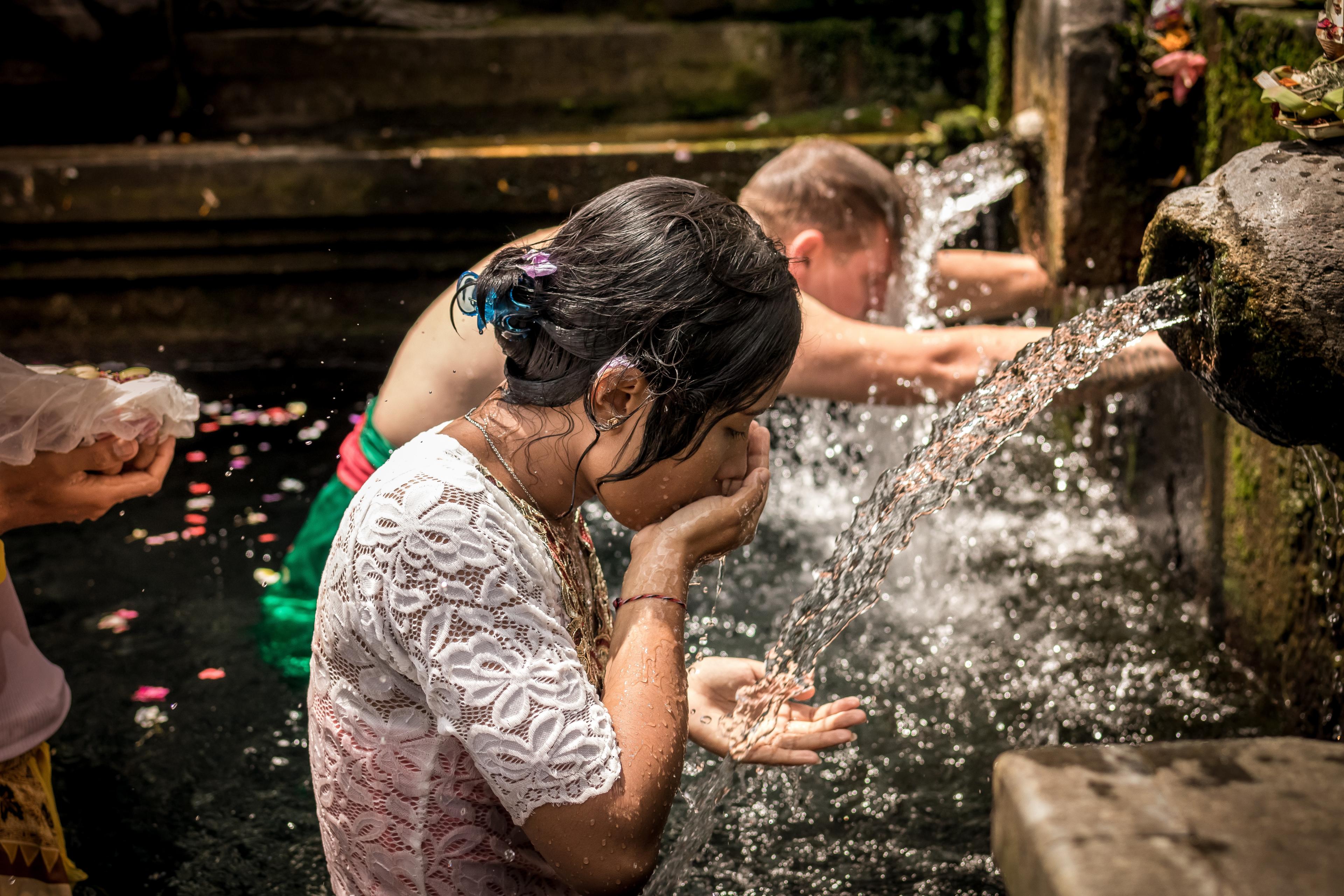 People praying in the Tirta Empul temple (Bali, Indonesia), submerged to the waist in water and bowing before fountains that are pouring out water.