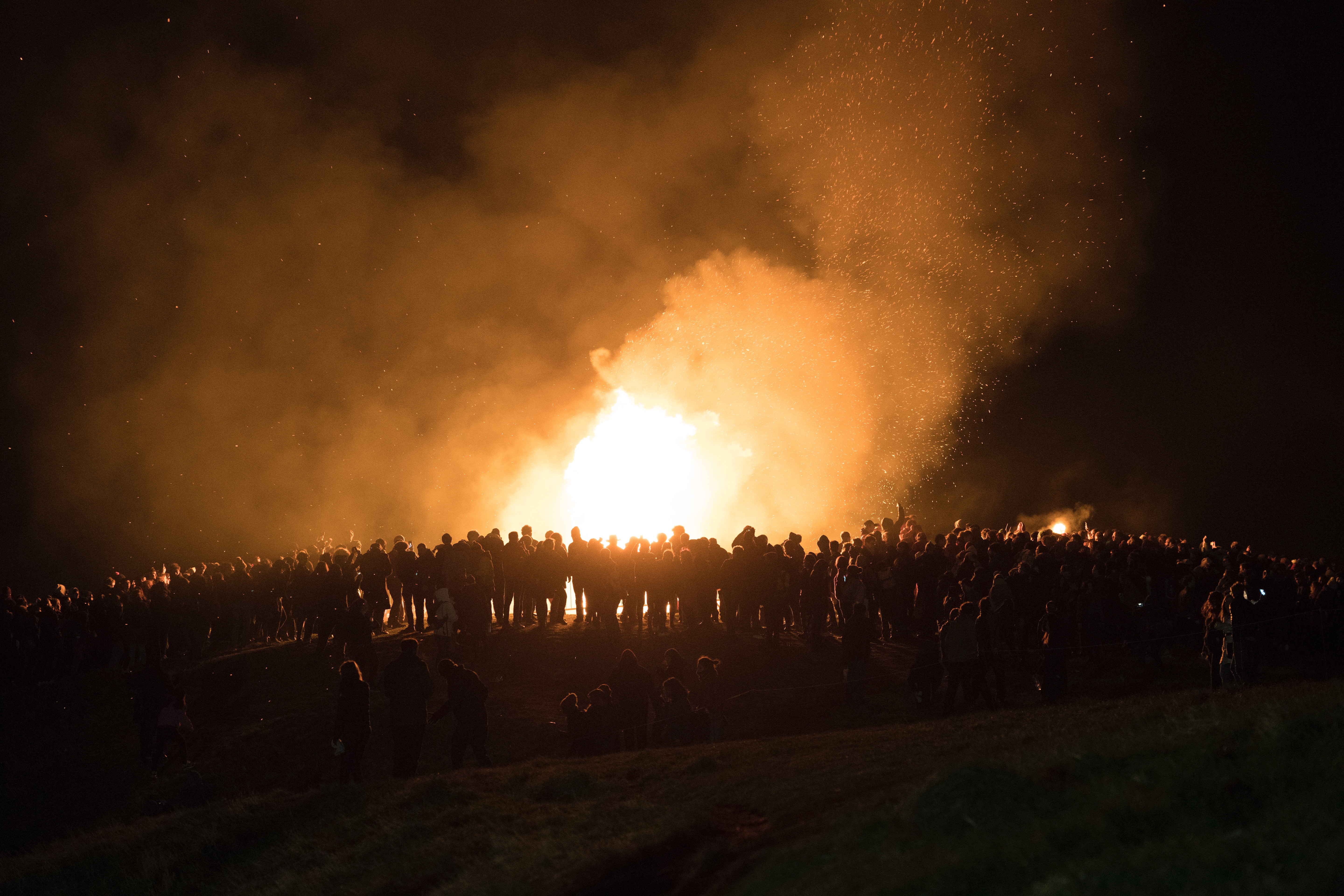 A large number of people are in silhouette against the blaze of a bonfire