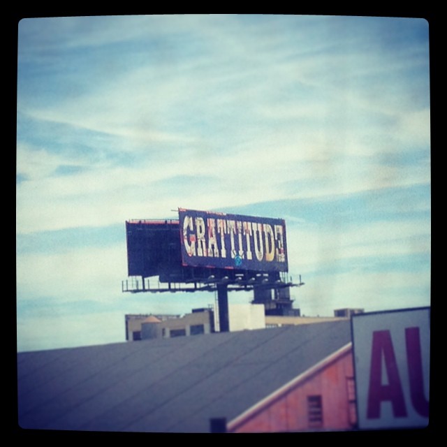 Against a blue sky, a billboard on top of a building says GRATITUDE
