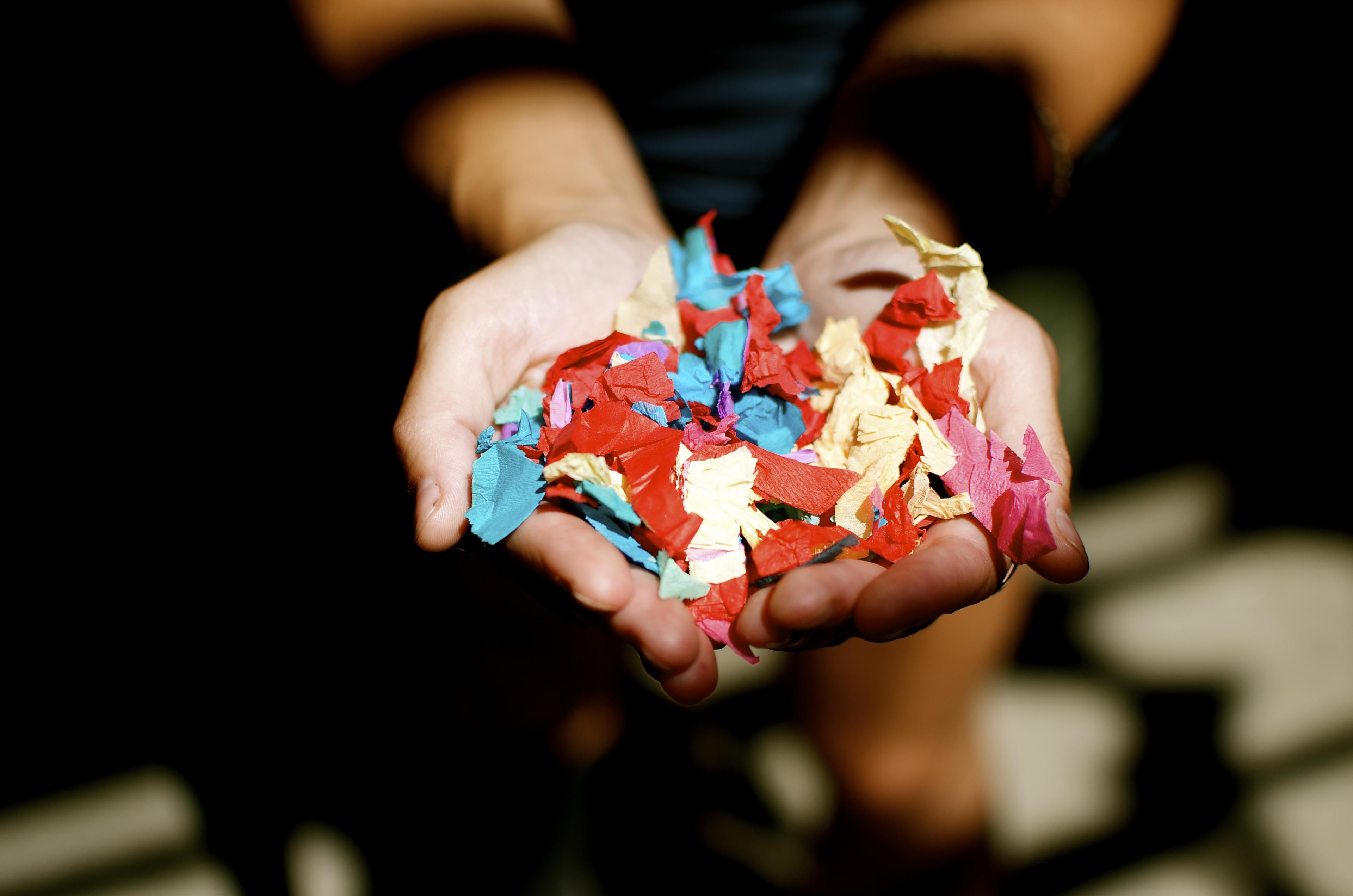 A person cups their hands to hold multi-colored confetti