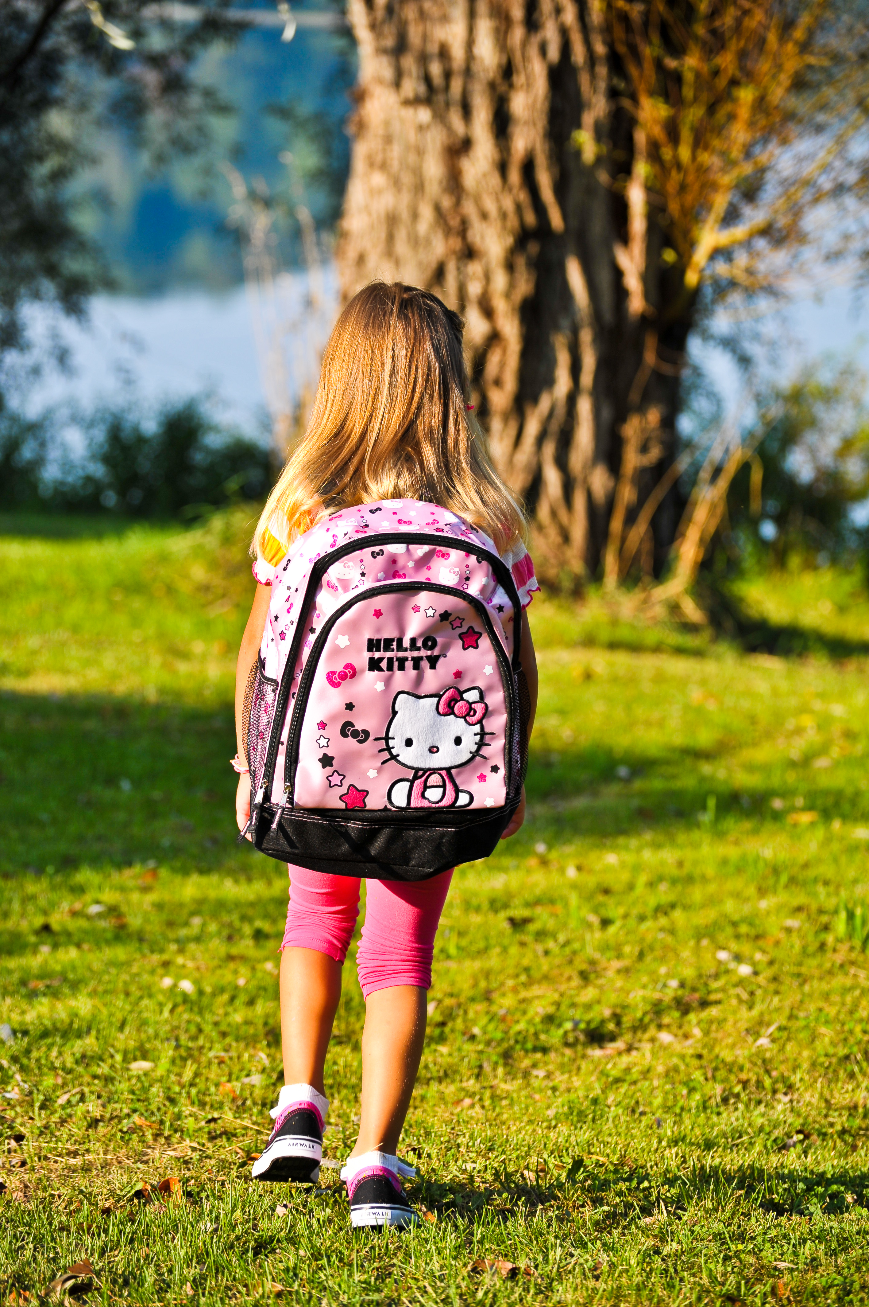 A young girl wears a large pink Hello Kitty backpack, in this photo taken from behind.