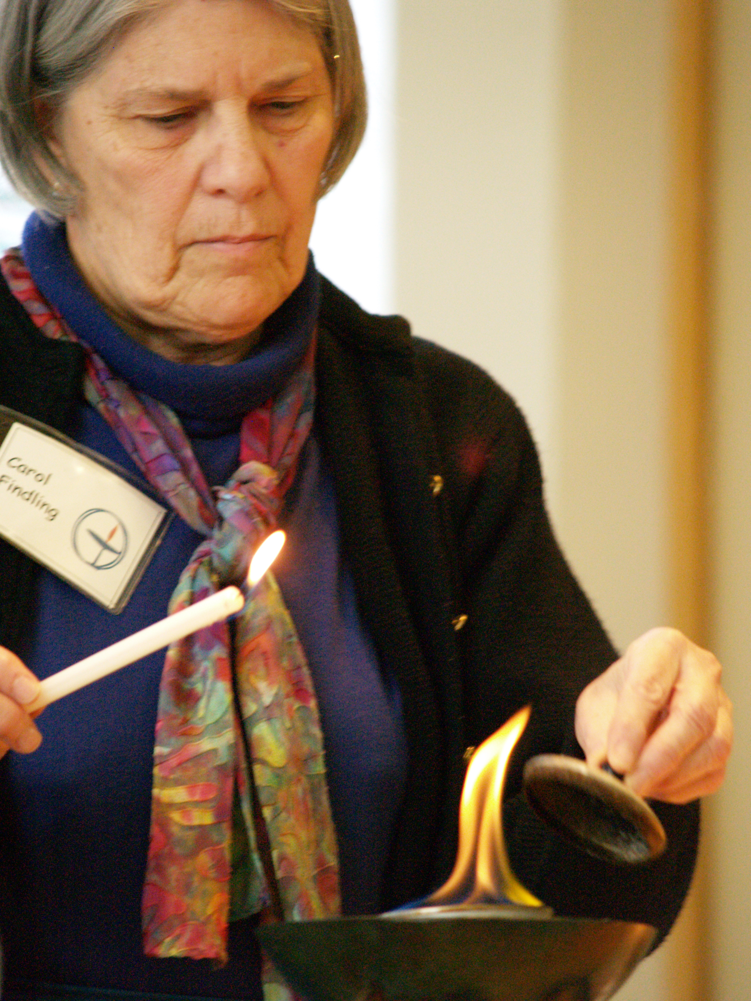 Holding a small lit candle, a UU named Carol lights a large chalice flame