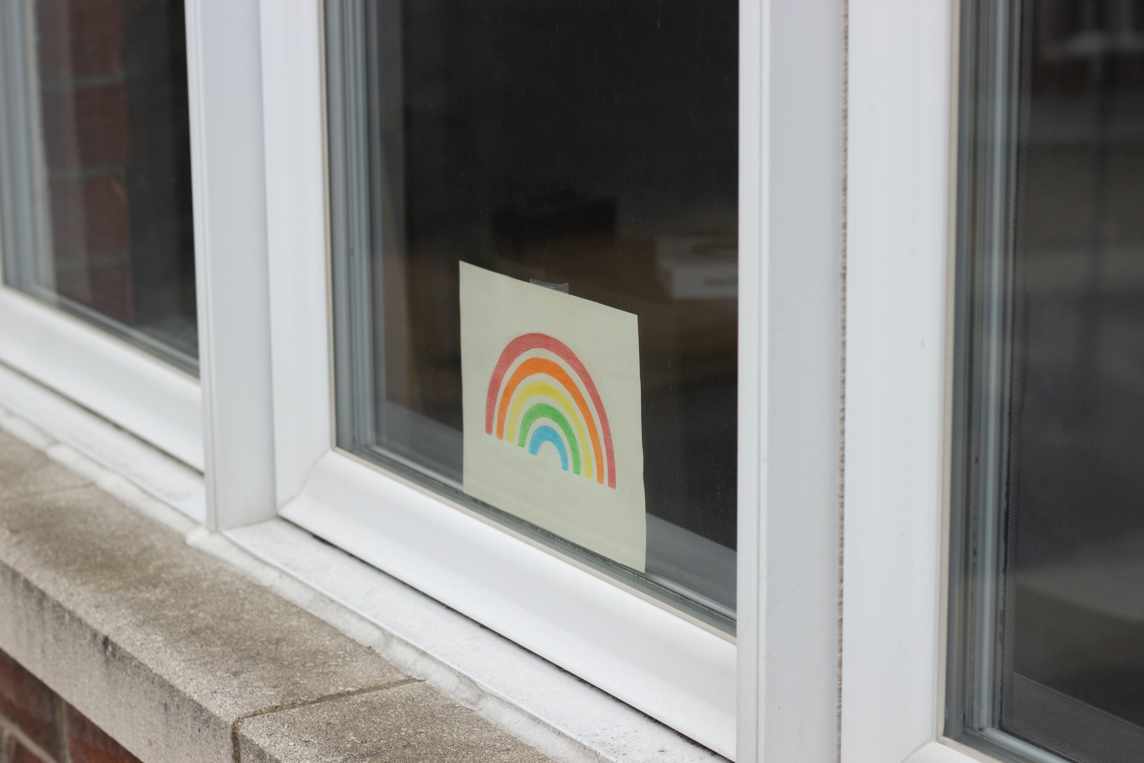 A rainbow, drawn on a piece of paper, inside a house window.