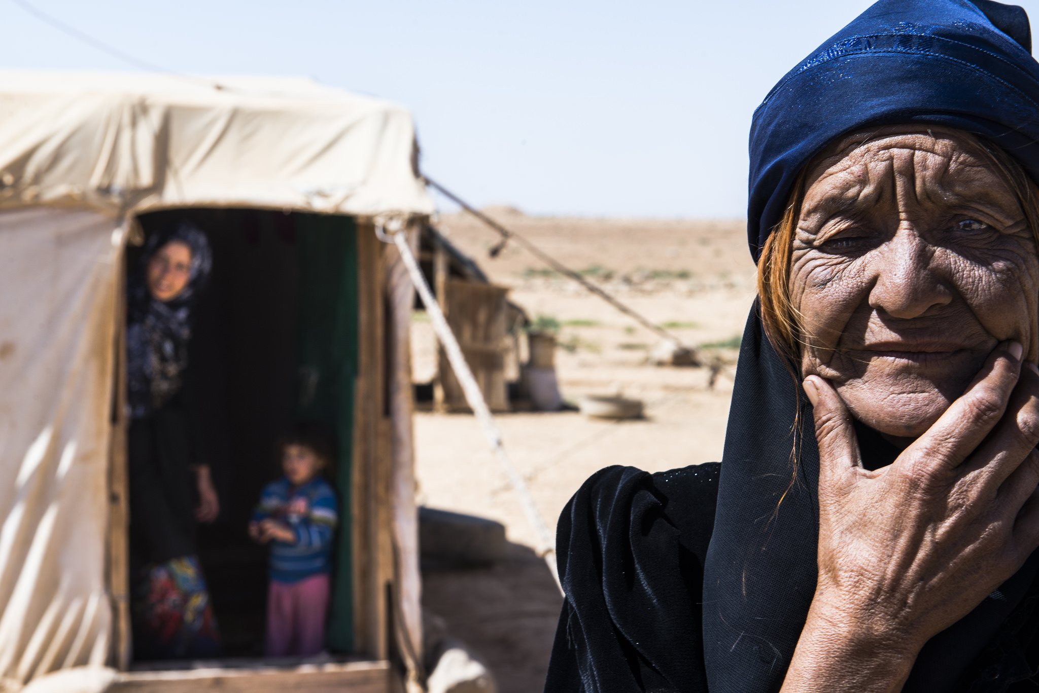 A Syrian refugee at a camp in Jordan looks into the camera; behind her, children look out from a tent. 
