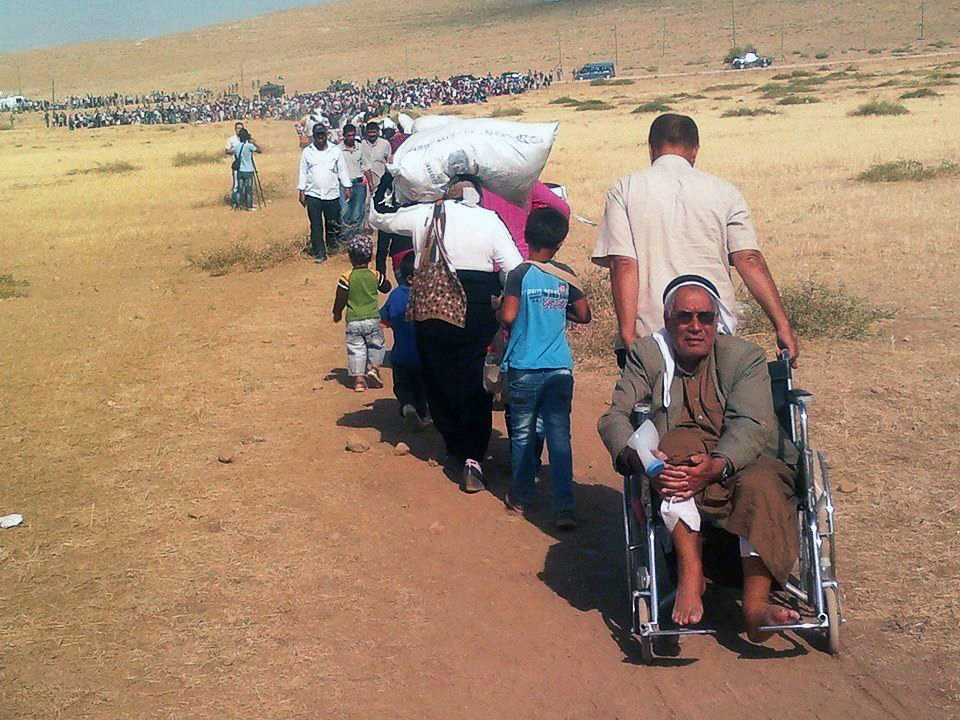 A long line of Syrian Kurdish refugees travel across a parched field intoto Turkey