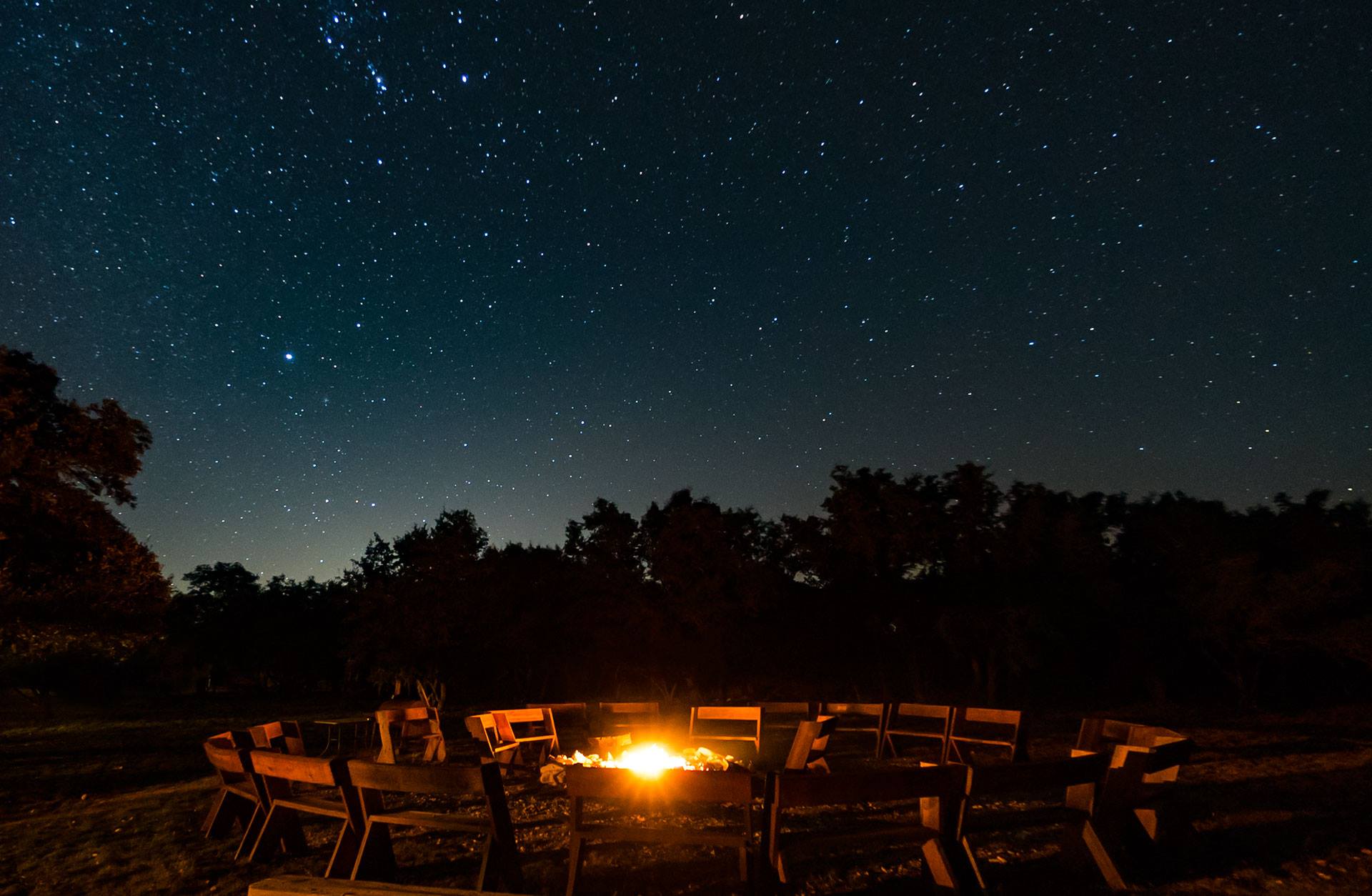 a fire is surrounded by chairs under a starry night sky