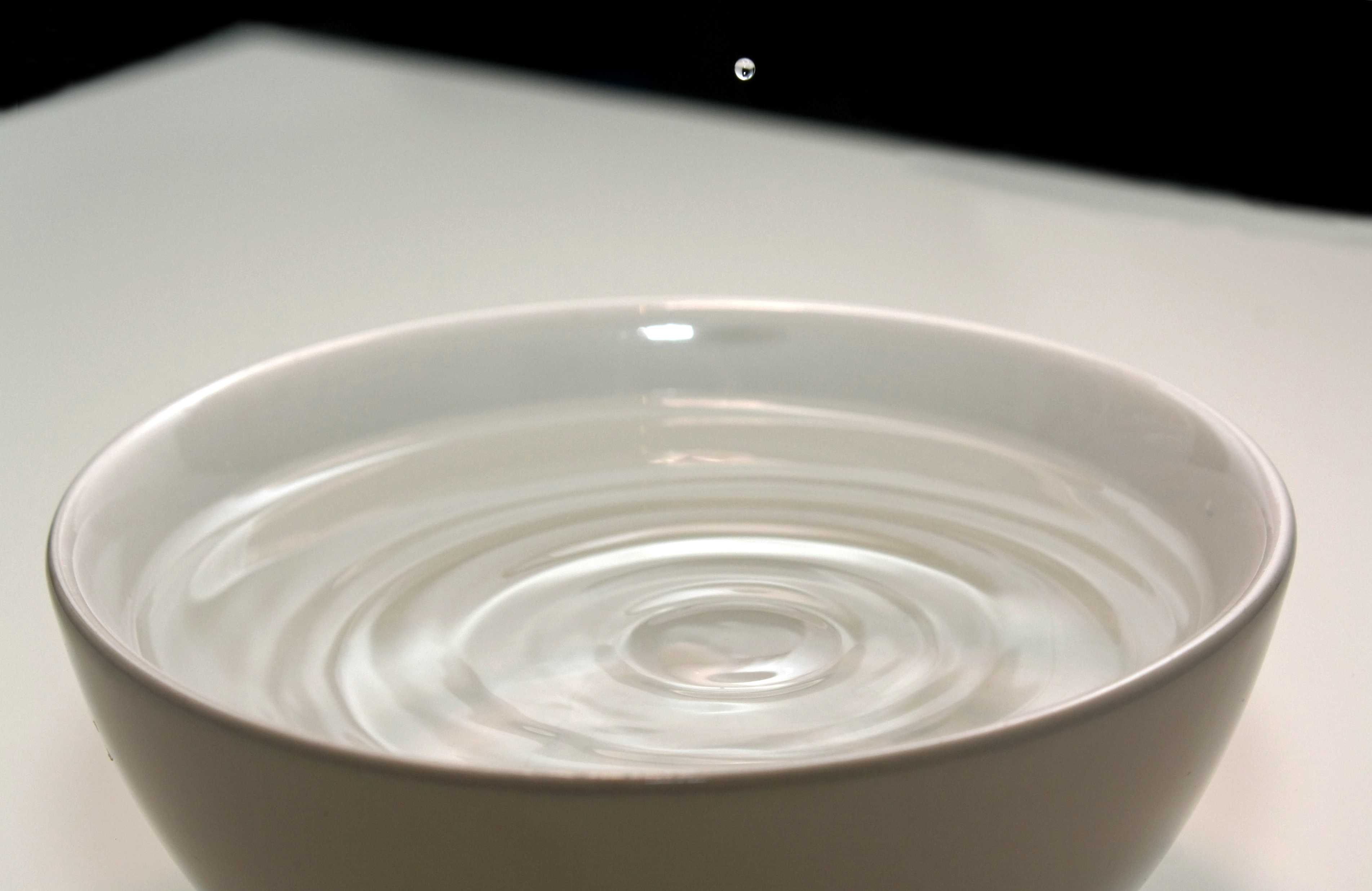 A tiny drop of water bouncing off of the surface of water in a bowl.