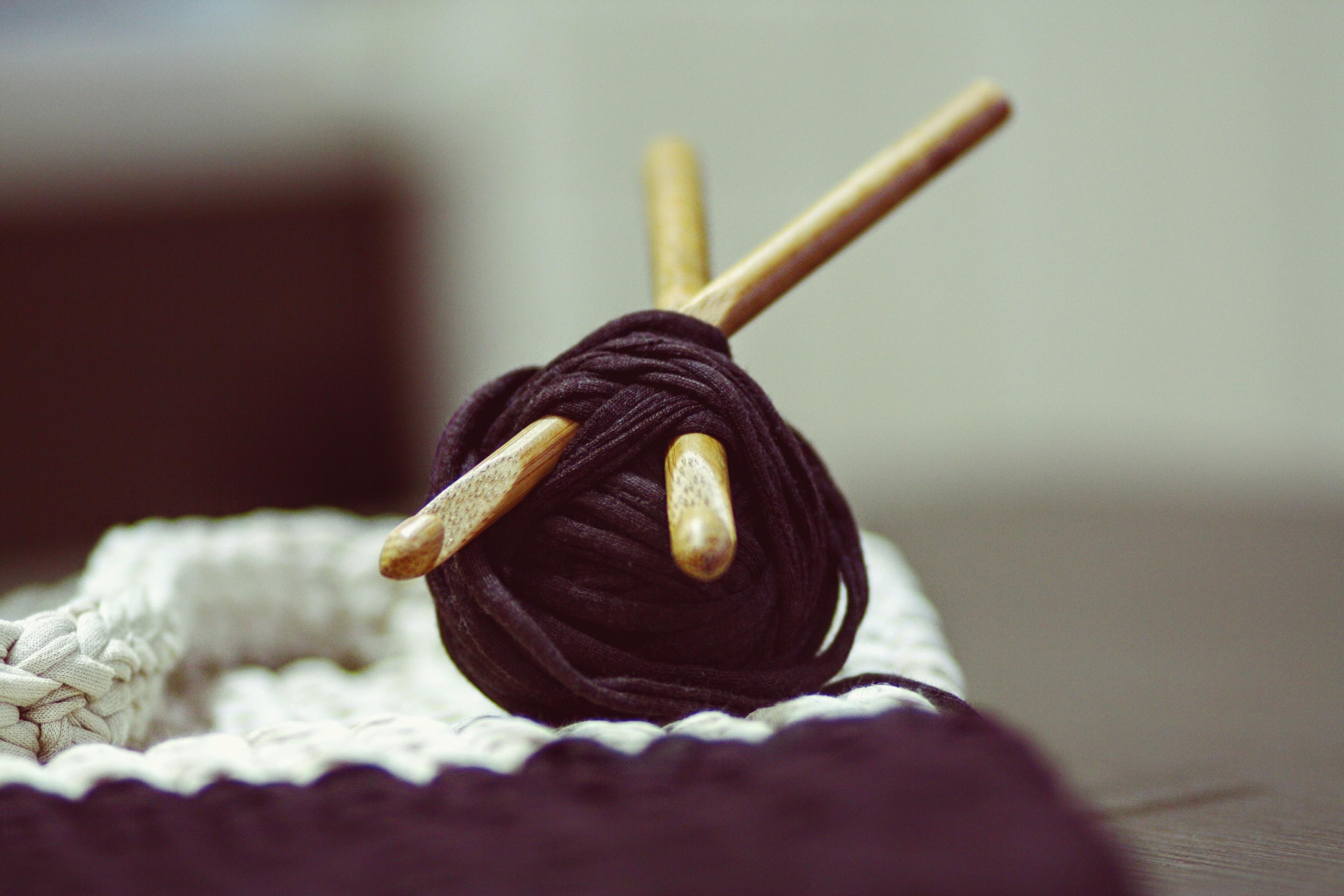Two wooden knitting needles plunged into a ball of thick purple yarn