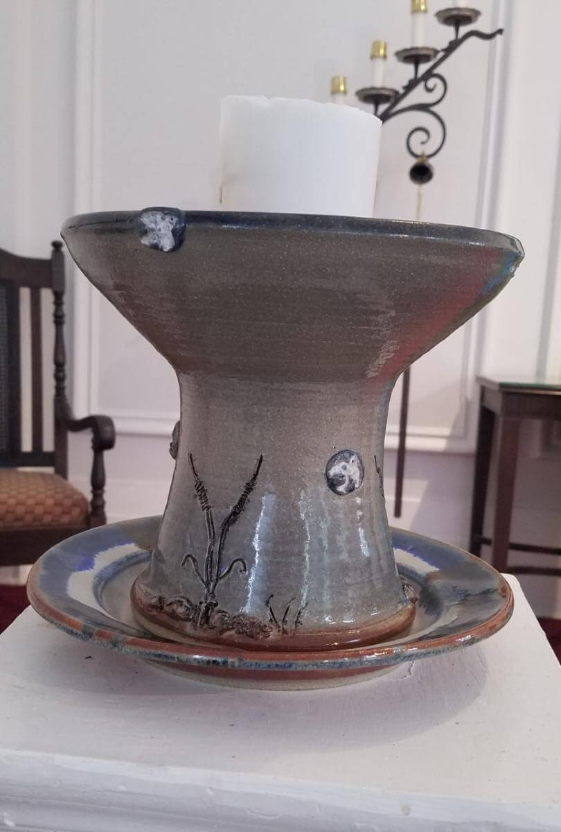 A chalice, by Nebraska potter Thomas Hamilton, inspired by the local landscape of rivers and prairie -- river glaze colors, edge plants and stones, birds, and three rivers meeting in the cup.