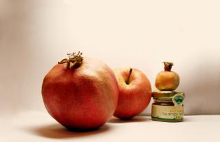An apple, two pomegranates, and a small jar of honey with a label printed in Hebrew.