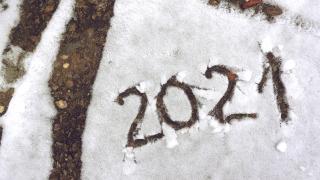 "2021" is written in the snow on a gravel surface outdoors.