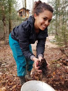 Photo of Brooke Bridges in the woods holding a handful of soil and smiling at the camera