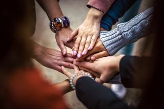 A close-up of the stacked hands of about five people, standing in a circle.