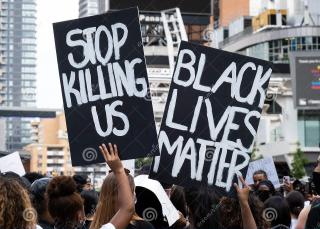Black protestors with their back to the camera hold up black signs with white hand-painted writing, one reading "Stop Killing Us" and the other reading "Black Lives Matter"