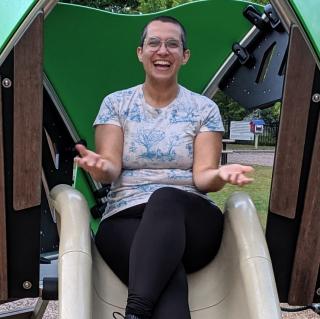 Lóre Stevens smiles while sitting at the top of a playground slide
