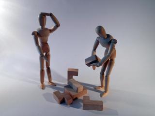 Two wooden people try to put together 3-D wooden puzzle