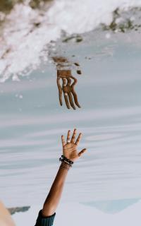 reflection of hand reaching into a body of water