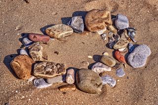 a circle of smoothed beach rocks sits in a circle on the sand