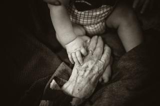 A black-and-white photo of an infant, whose hand is holding the gnarled hand of his great-grandmother.